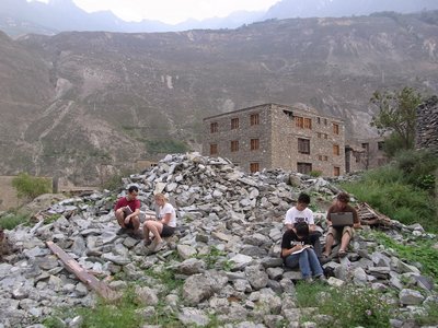 Students drawing sitting on a pile of rocks and rubble with mountains in the background