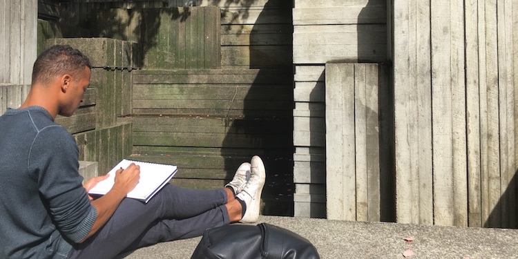 student sits with notebook in hand and sketches a concrete colonade