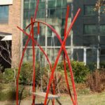 Swing constructed out of red metal poles and wooden swing