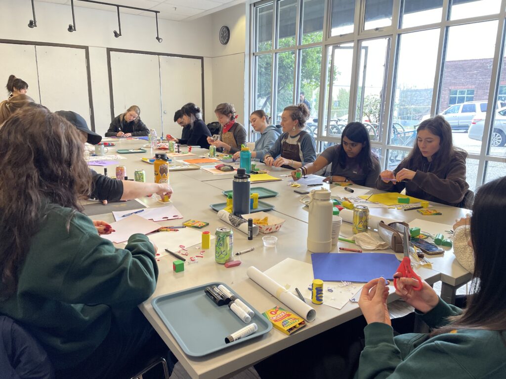 Large group of participants all sit together at a long rectangular table with crayons and paper