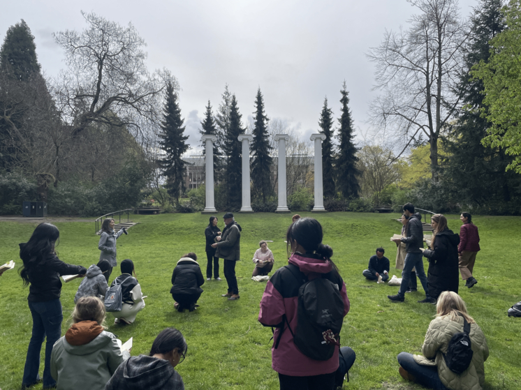 students sitting on green lawn with white columns as backdrop