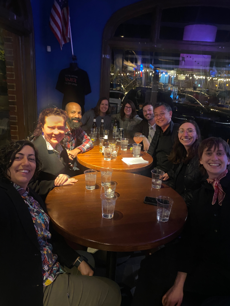 People gathered around a table inside a bar all facing the camera