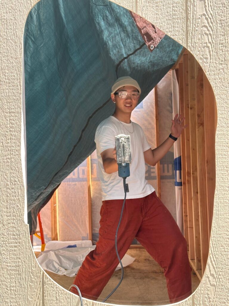 student holding a power tool working on tiny house